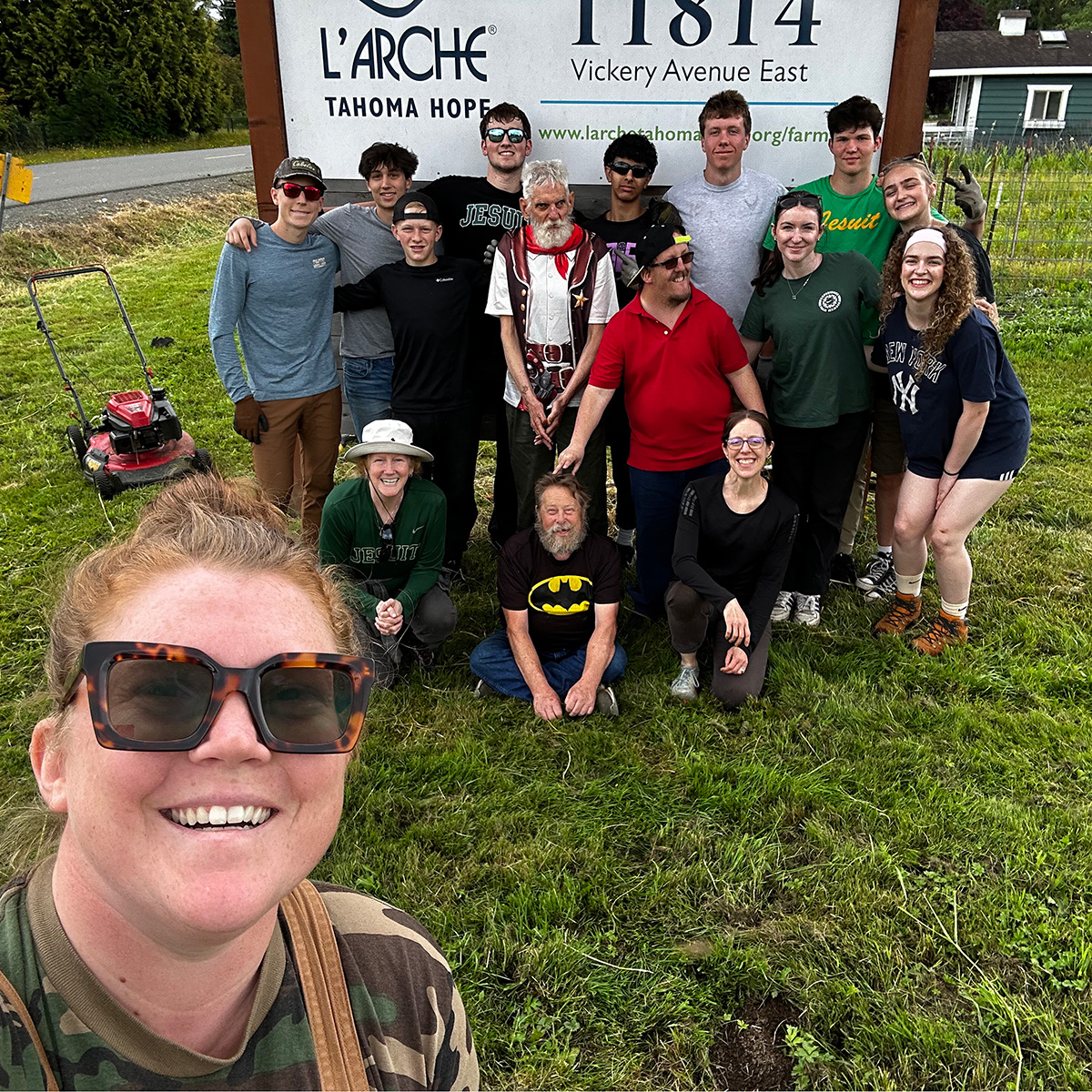 Group smiling in front of L'Arche Farm and Gardens sign. 