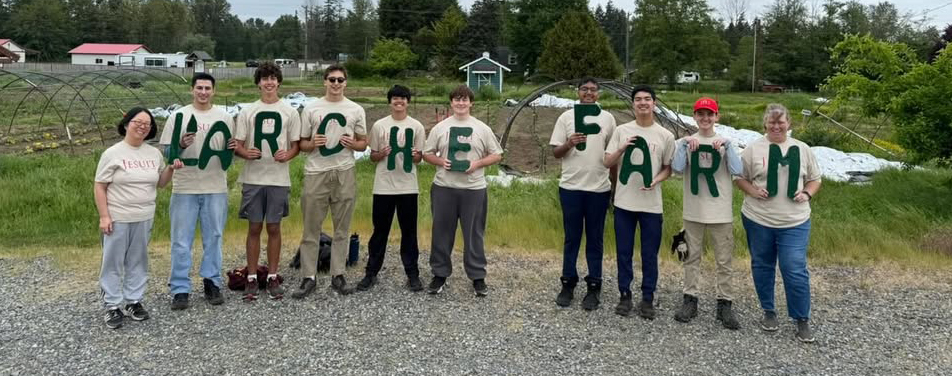 School group holding L'Arche Farm sign while standing outside. 